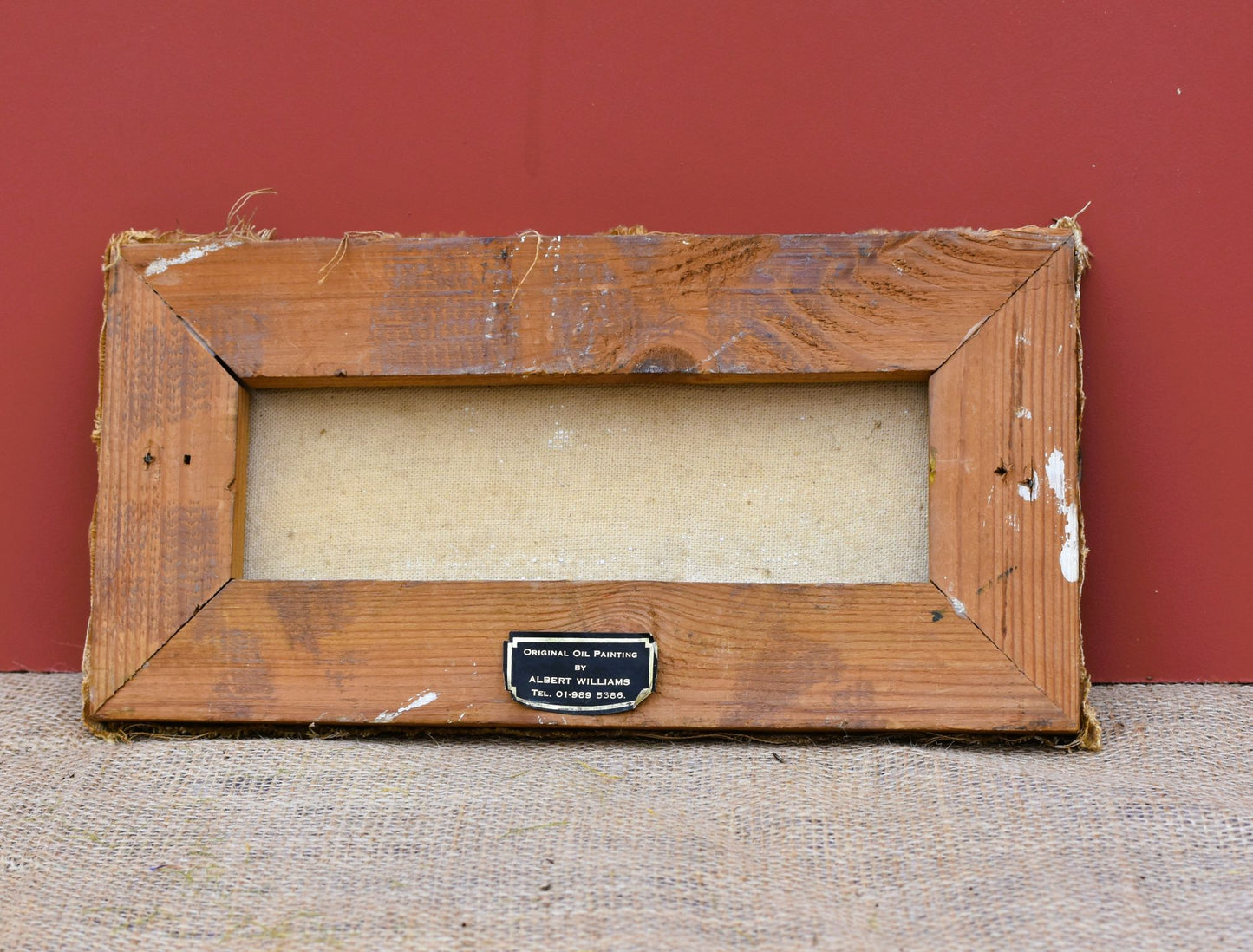Worn wooden picture frame with a label on a textured surface and red background