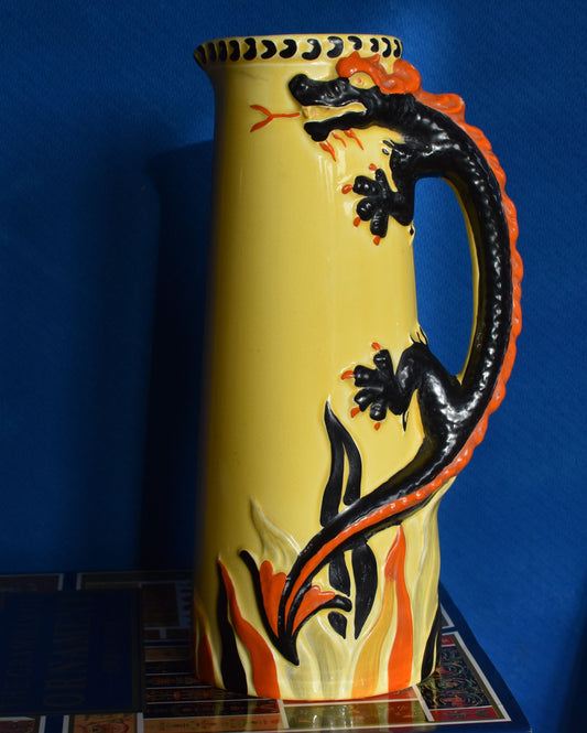 A tall yellow art deco jug decorated with a hand painted black and red dragon. The dragon's body forms the jug handle.