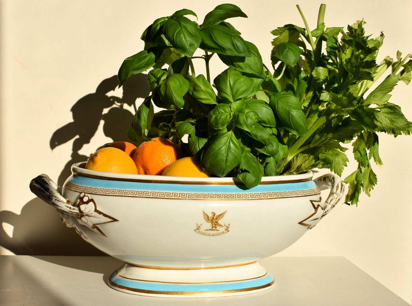 A large white tureen is decorated with an eagle crest that says Sursum Specto. Blue bands run at the top and bottom and there is gold decoration around the rims and handles