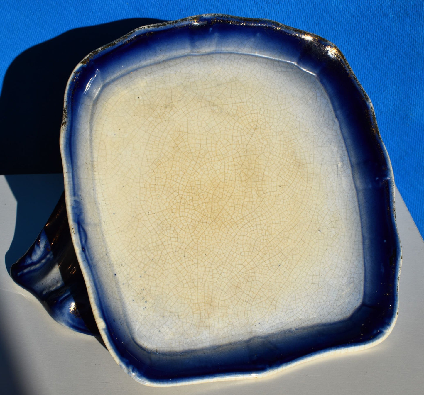 The base of the dish has a dark blue rim with gold gilding. the centre of the dish has crazing through the glaze