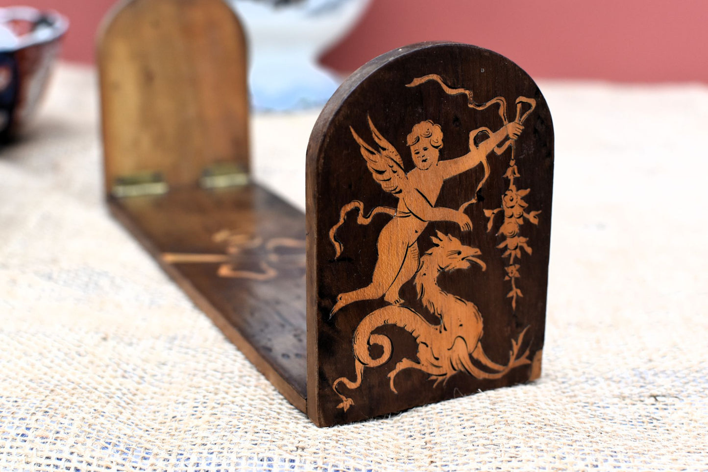 Wooden bookend with decorative design of a cherub and griffin or dragon on a textured surface.
