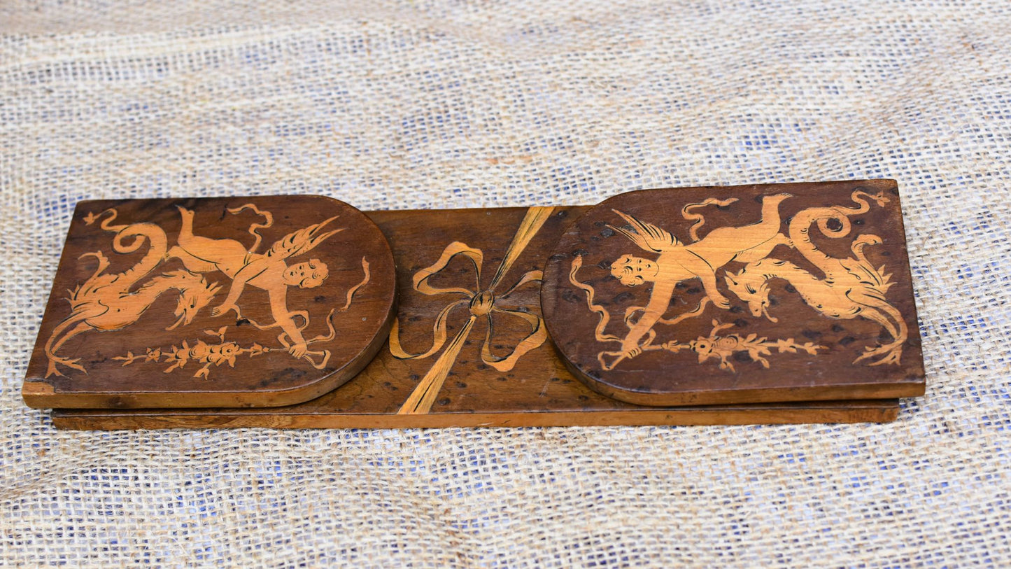 Wooden decorative panel with intricate carvings of cherubs and ribbons on a textured fabric background.