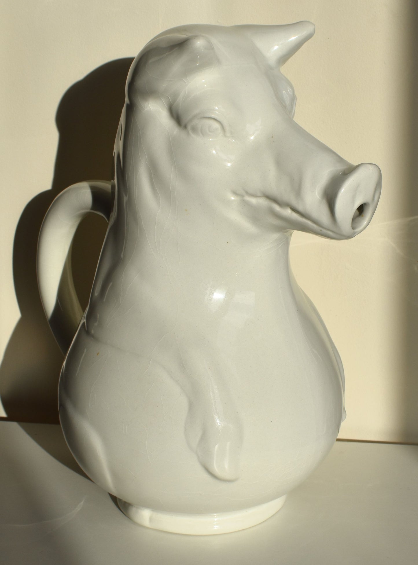 A large white jug is shaped like a pig sitting up, with its snout as the spout of the jug