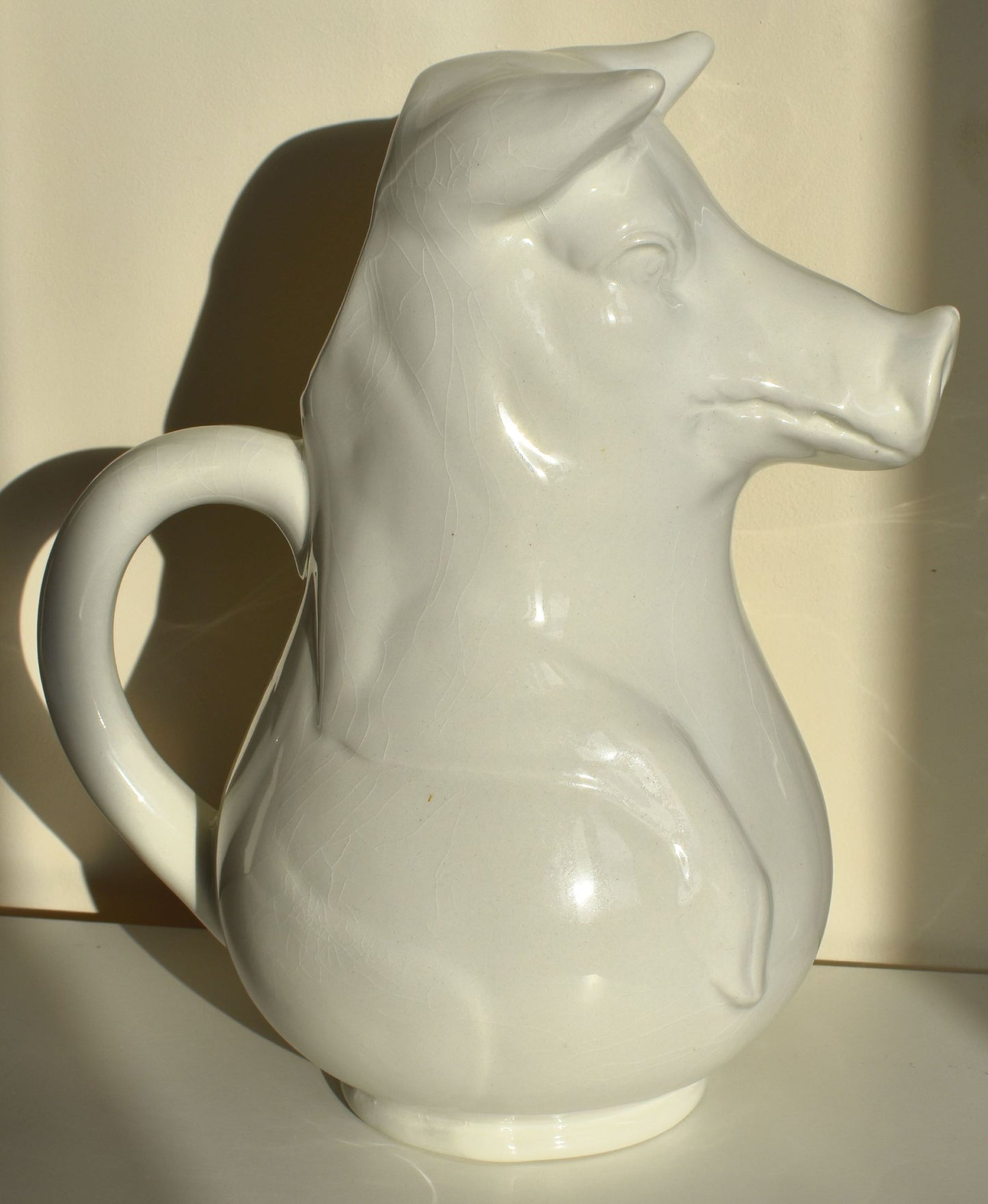 A large white jug is shaped like a pig sitting up, with its snout as the spout of the jug (Side view)