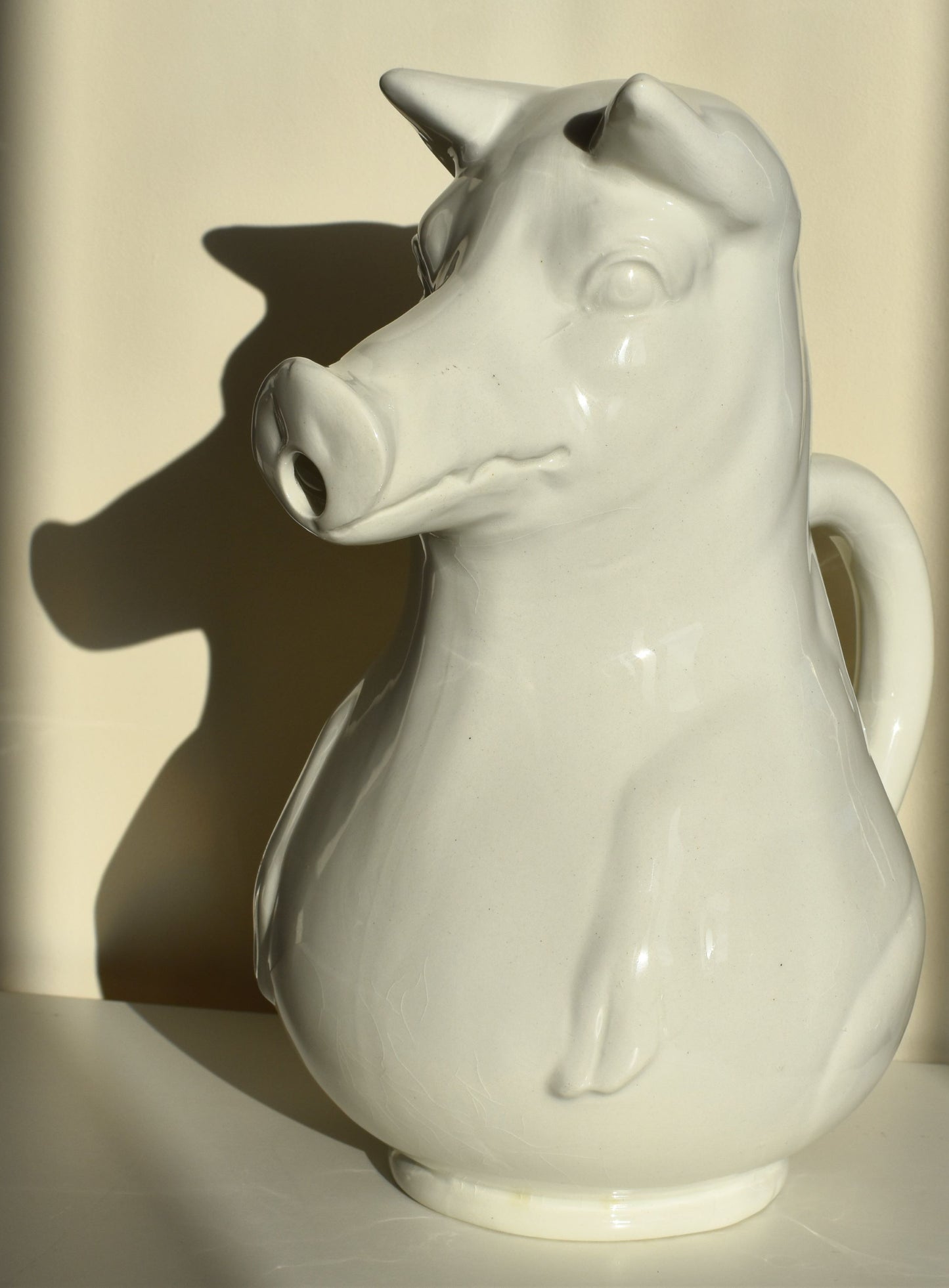 A large white jug is shaped like a pig sitting up, with its snout as the spout of the jug