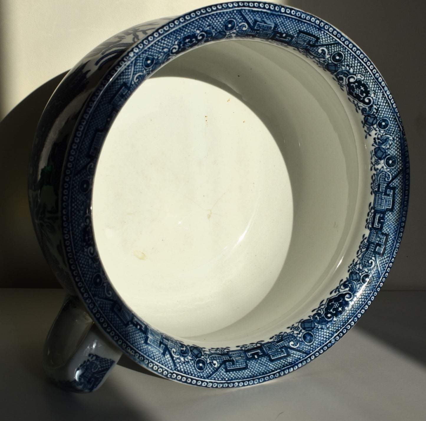 The rim of the chamber pot is decorated in intricate blue scrollwork and the inside of the pot is plain white