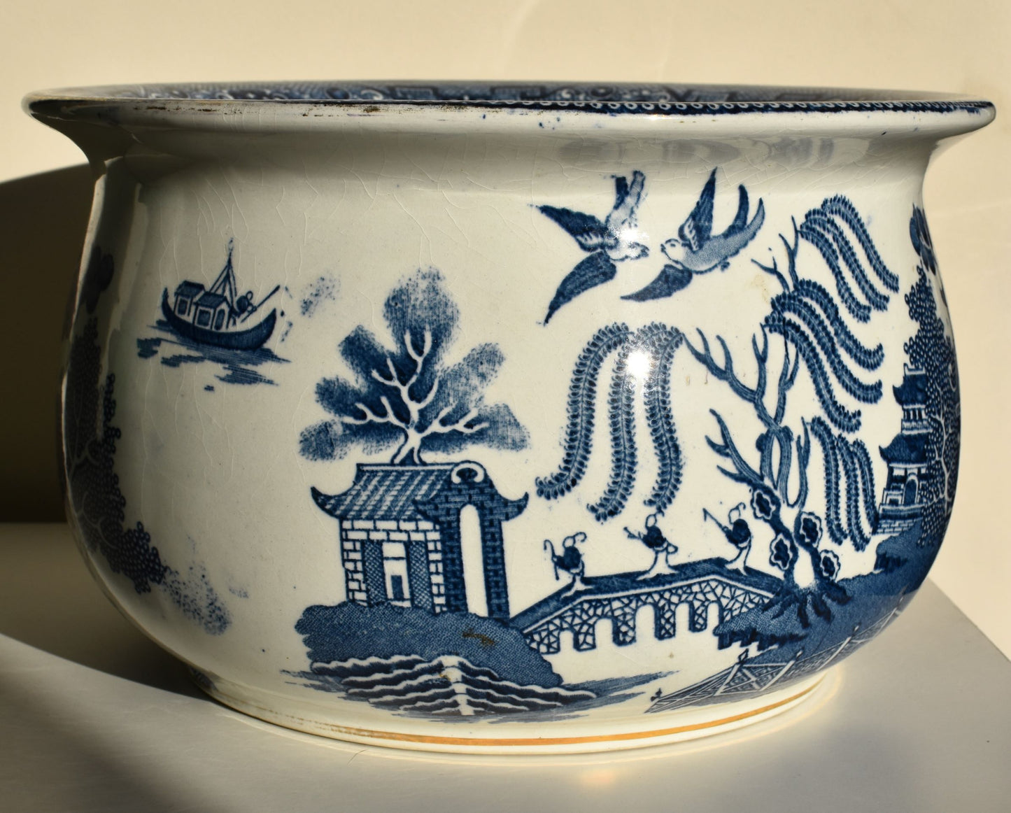 The large blue and white chamber pot is decorated with the traditional willow pattern (pagodas, willow tree, pair of birds)