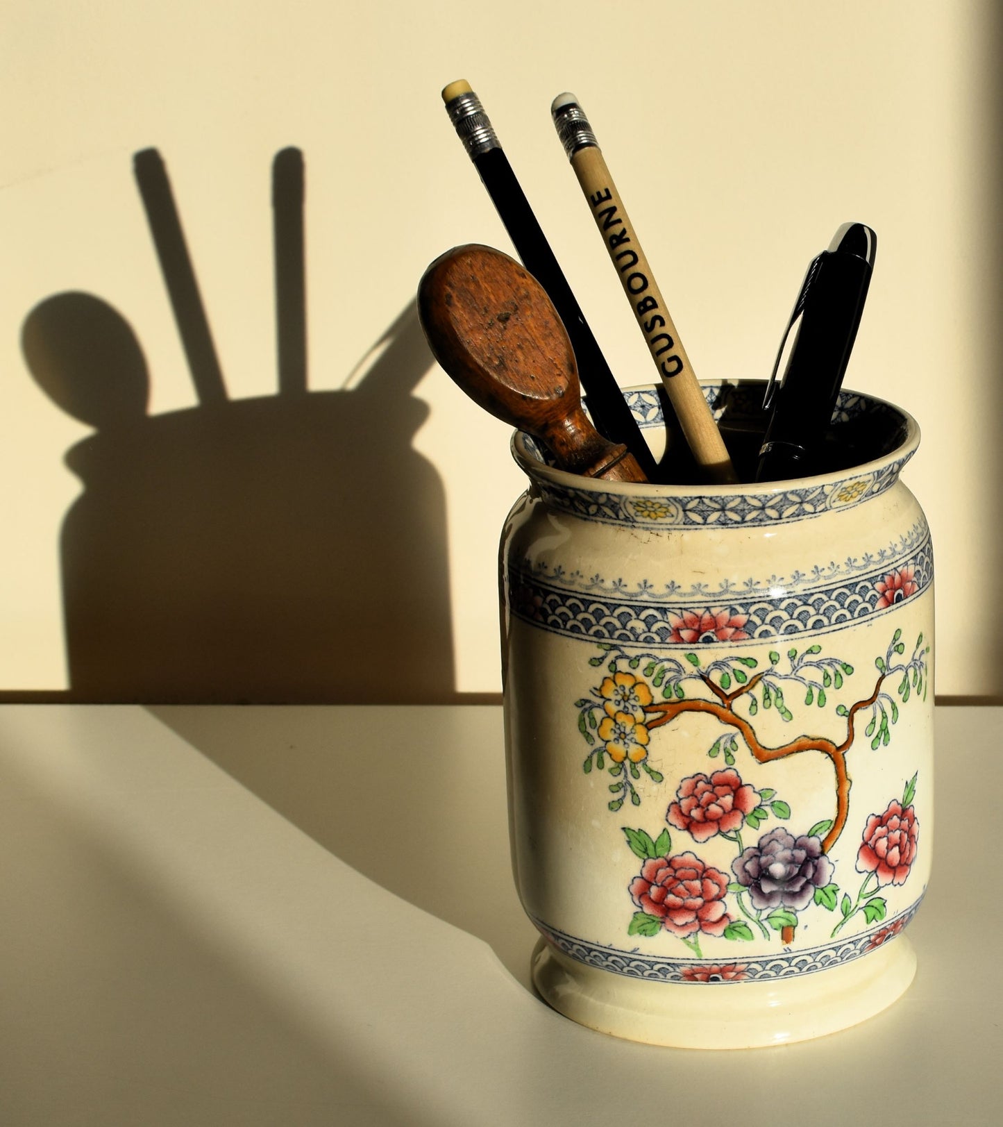 A cream pot is decorated with a branch with yellow flowers, with extra flowers in pink and purple.