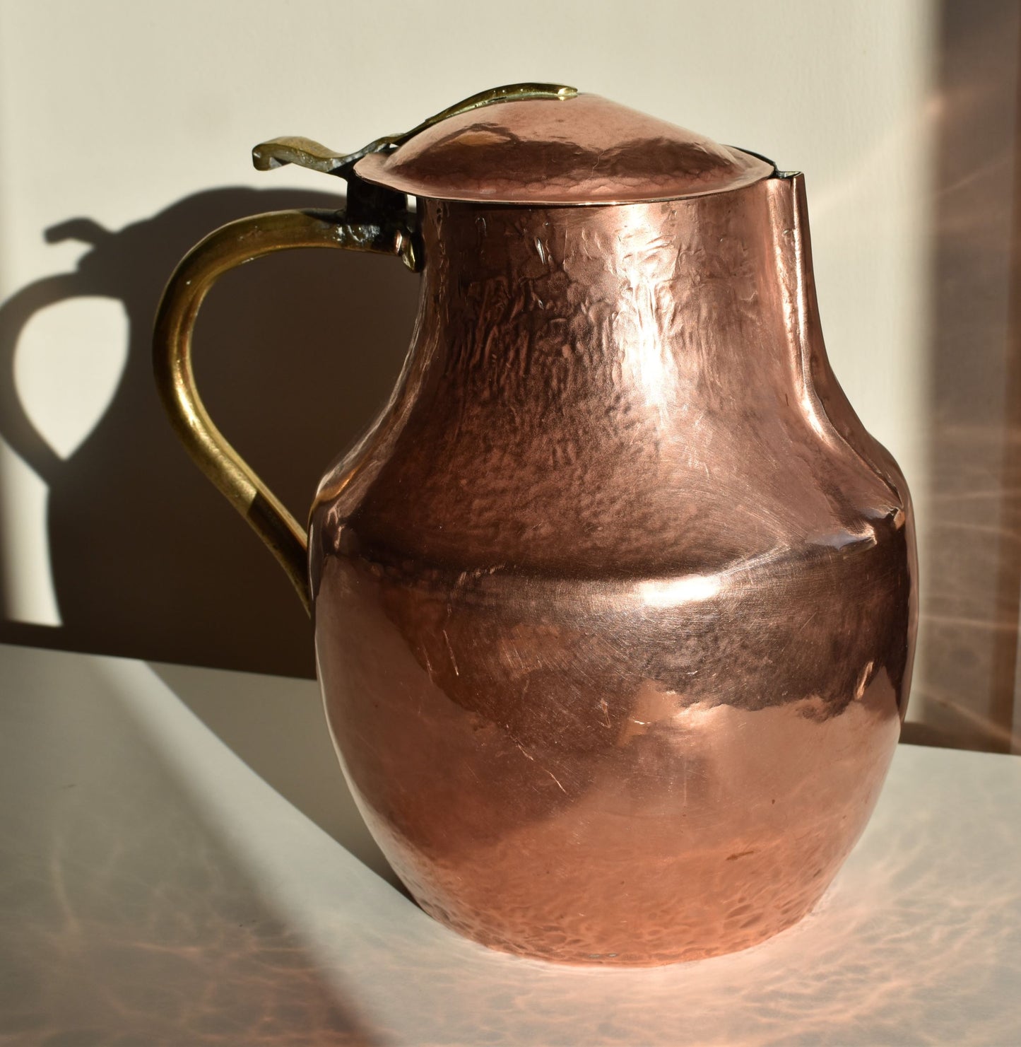 A large shiny copper jug, with copper hinged lid and brass handle