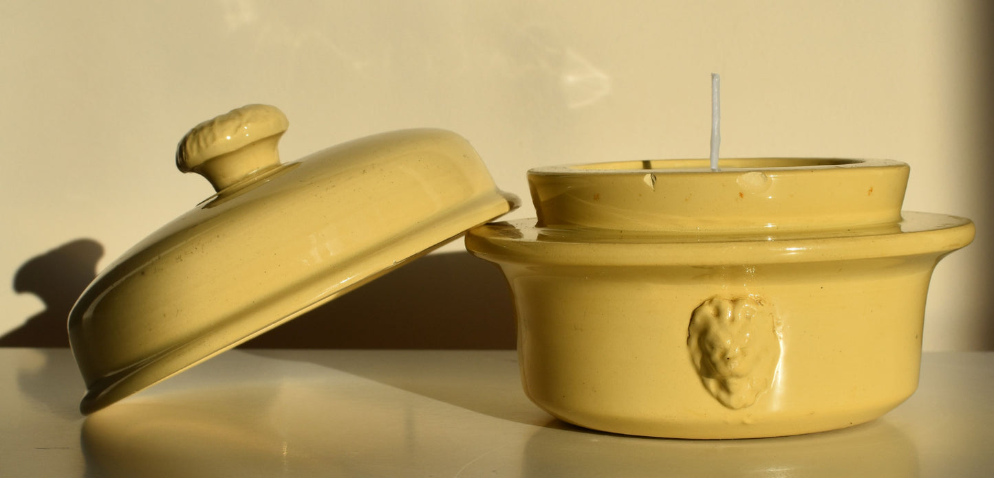 A cream pot with raised faces on the side has a candle wick showing at the top