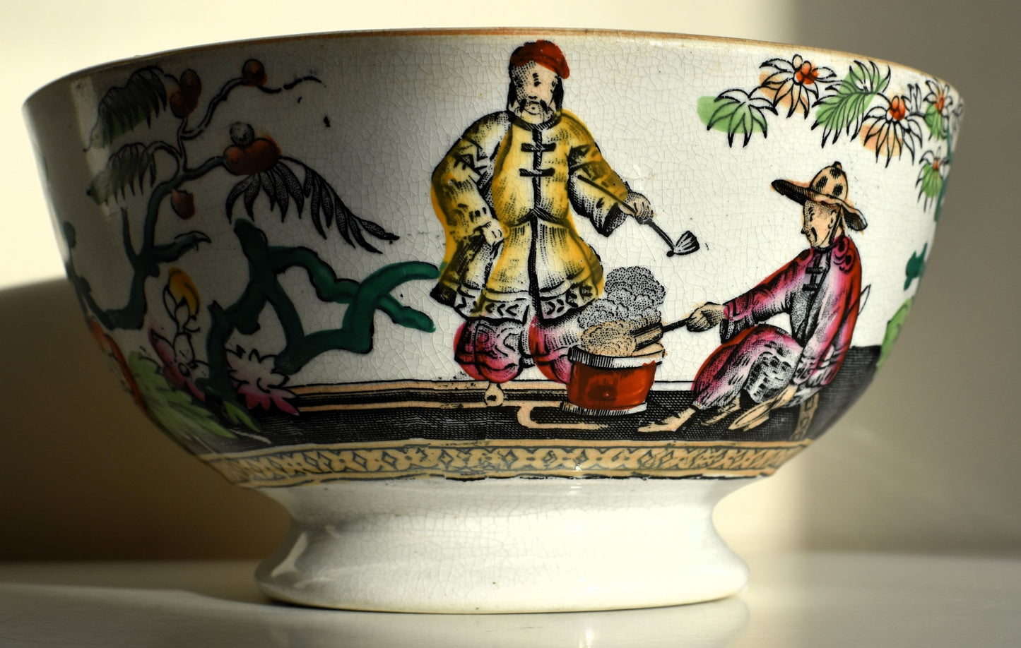 The bowl is decorated with chinoiserie figures and flowering plants