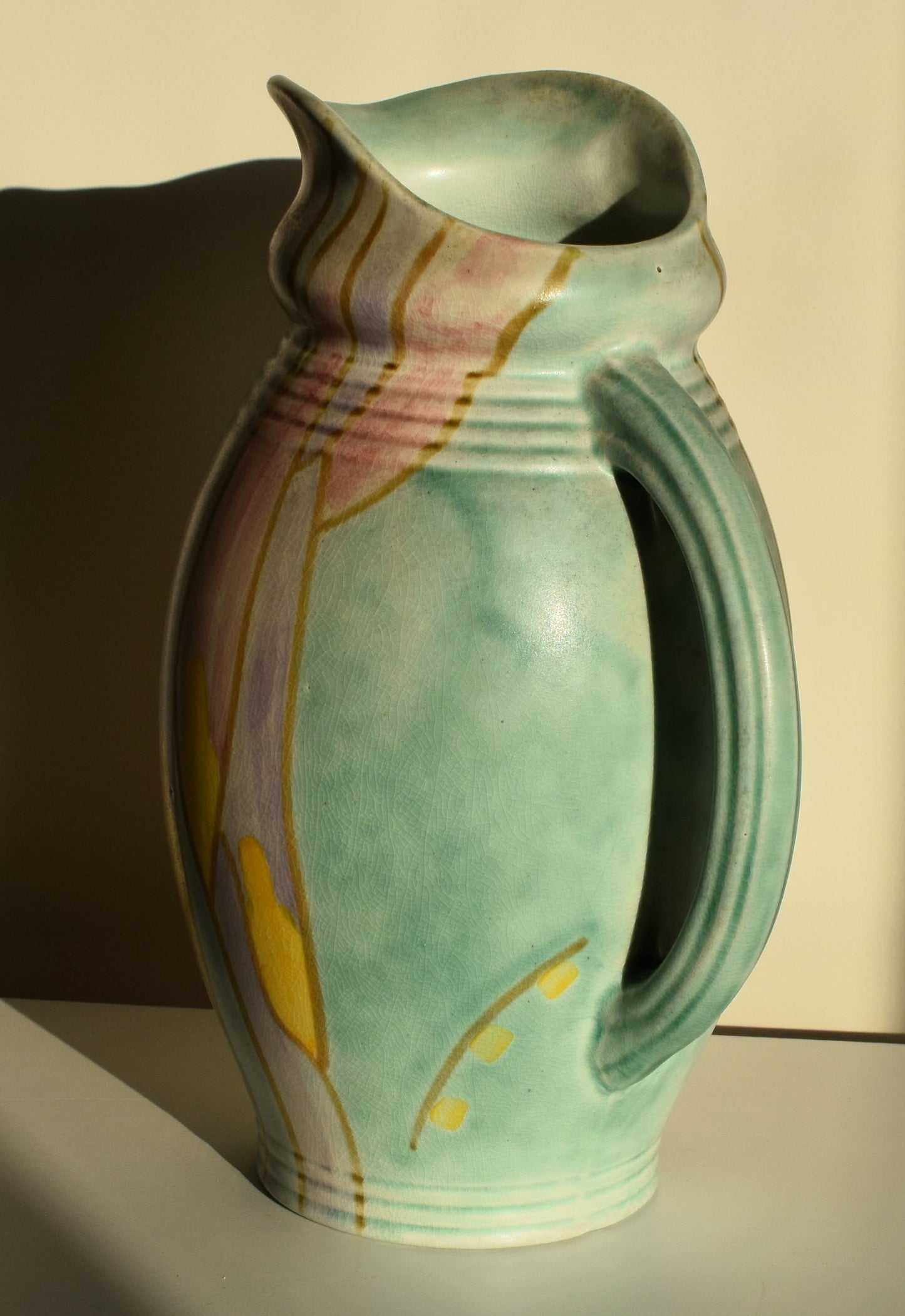 A green art deco jug is hand decorated with an abstract yellow, purple and pink floral