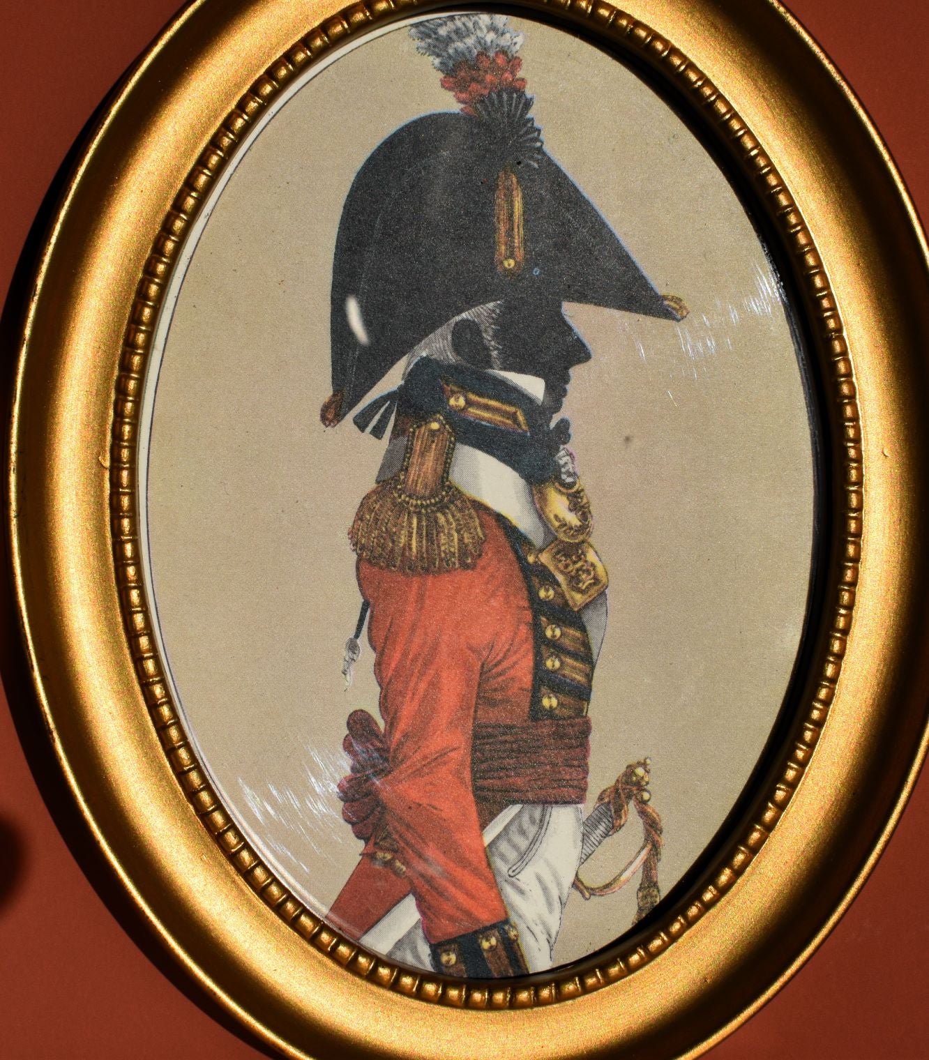the right painting has a silhouette in a red military coat, large black hat with a feather, all over gold details including buttons and epaulettes