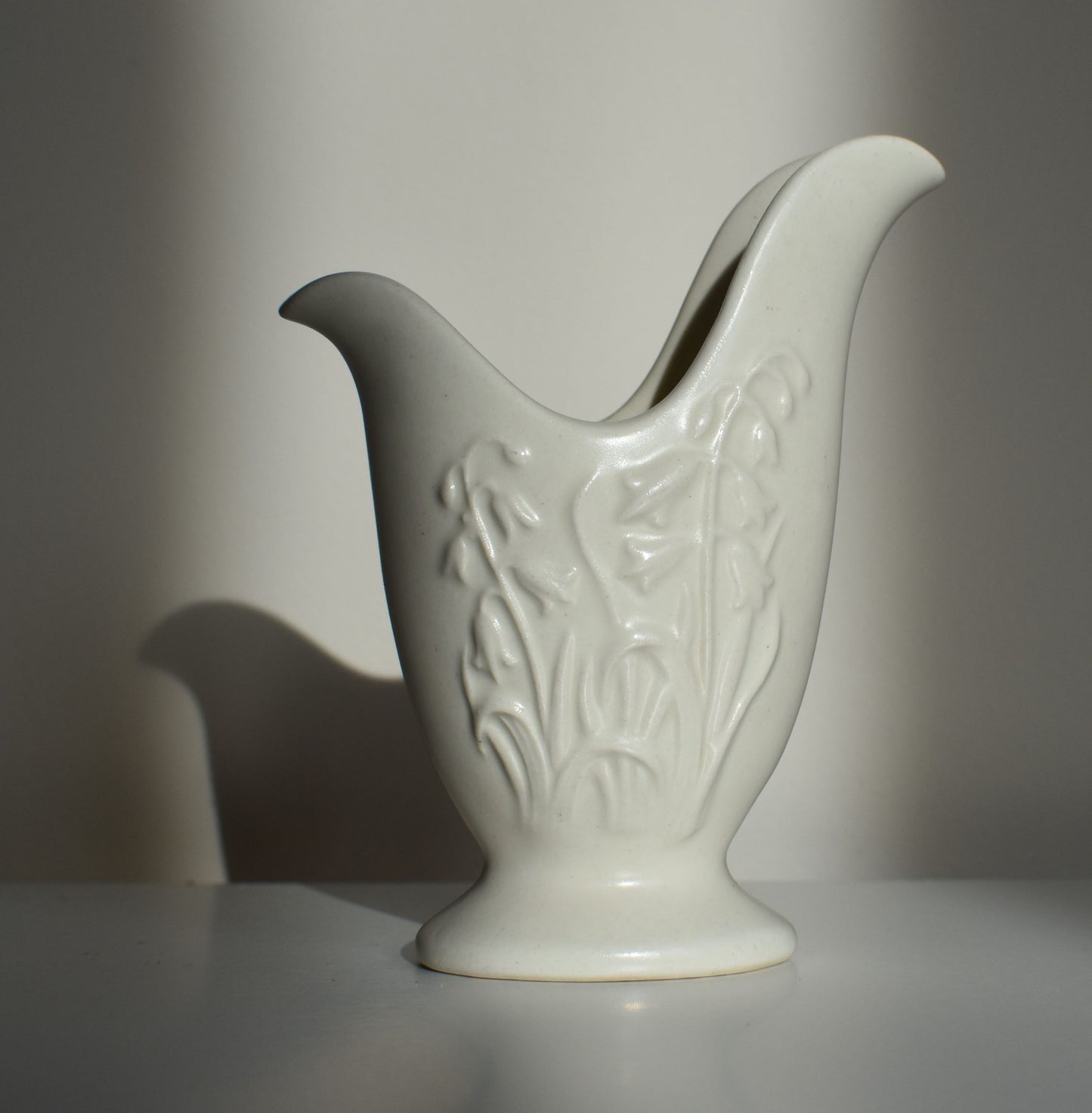A small white vase with bluebell flowers in relief