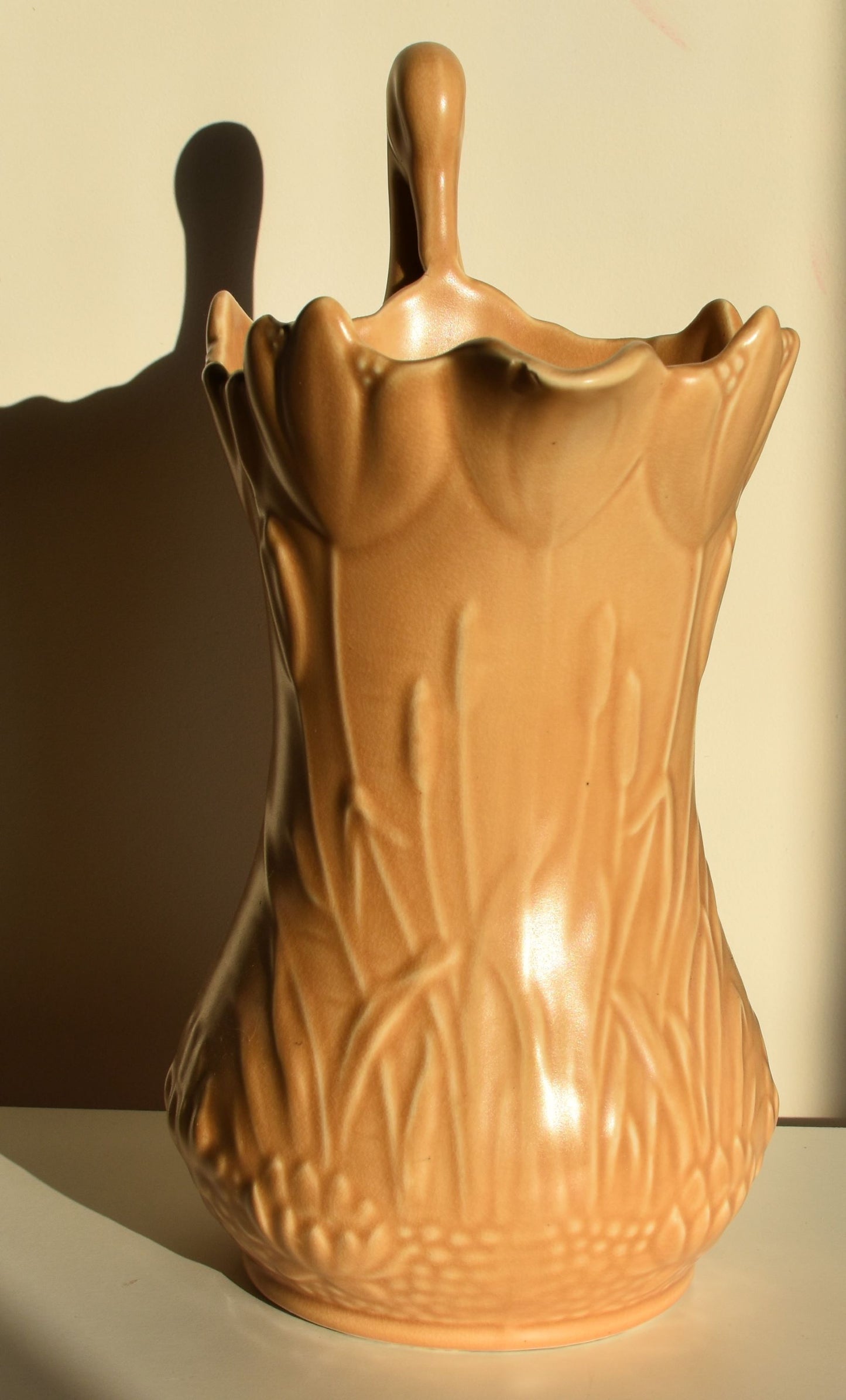 A caramel coloured vase decorated with lilies and tulips has a stork for a handle.