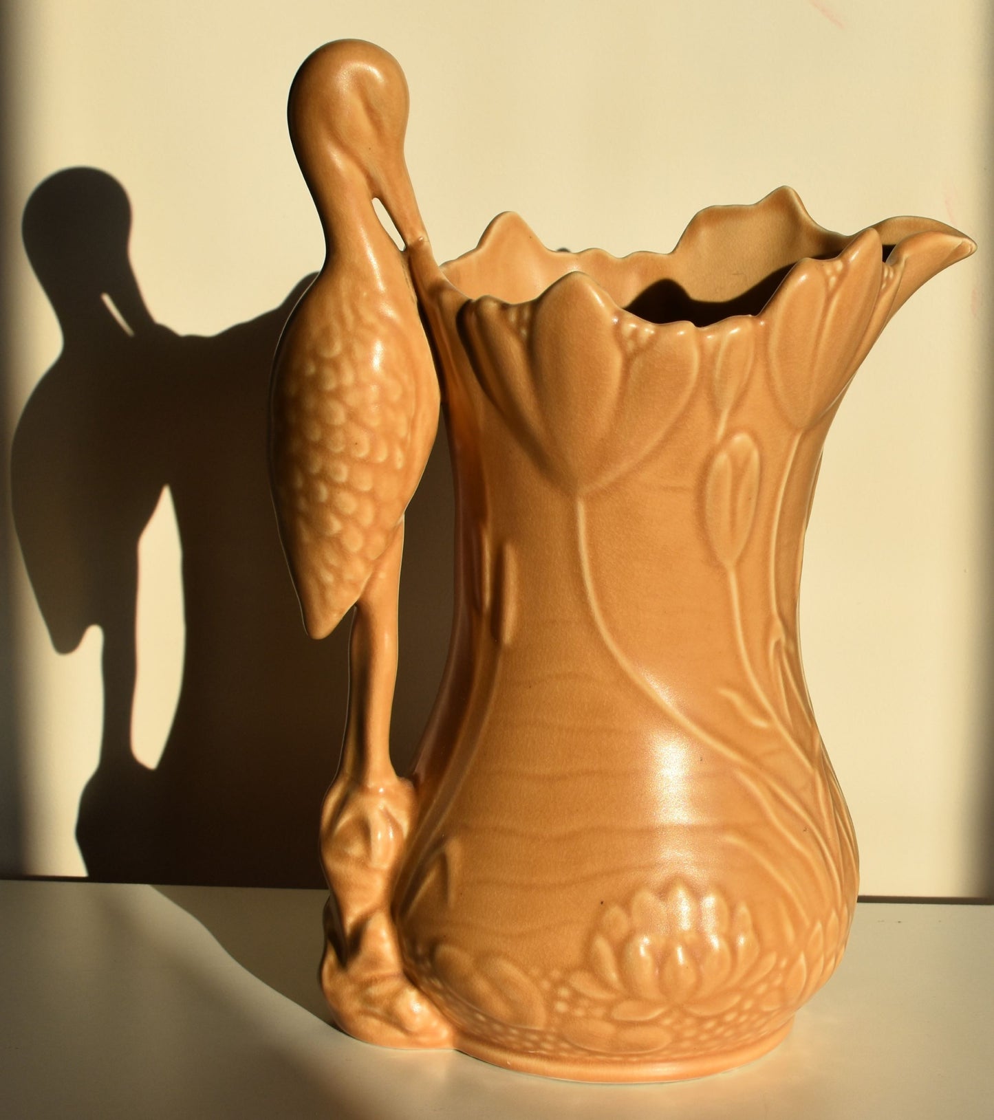 A caramel coloured vase decorated with lilies and tulips has a stork for a handle.