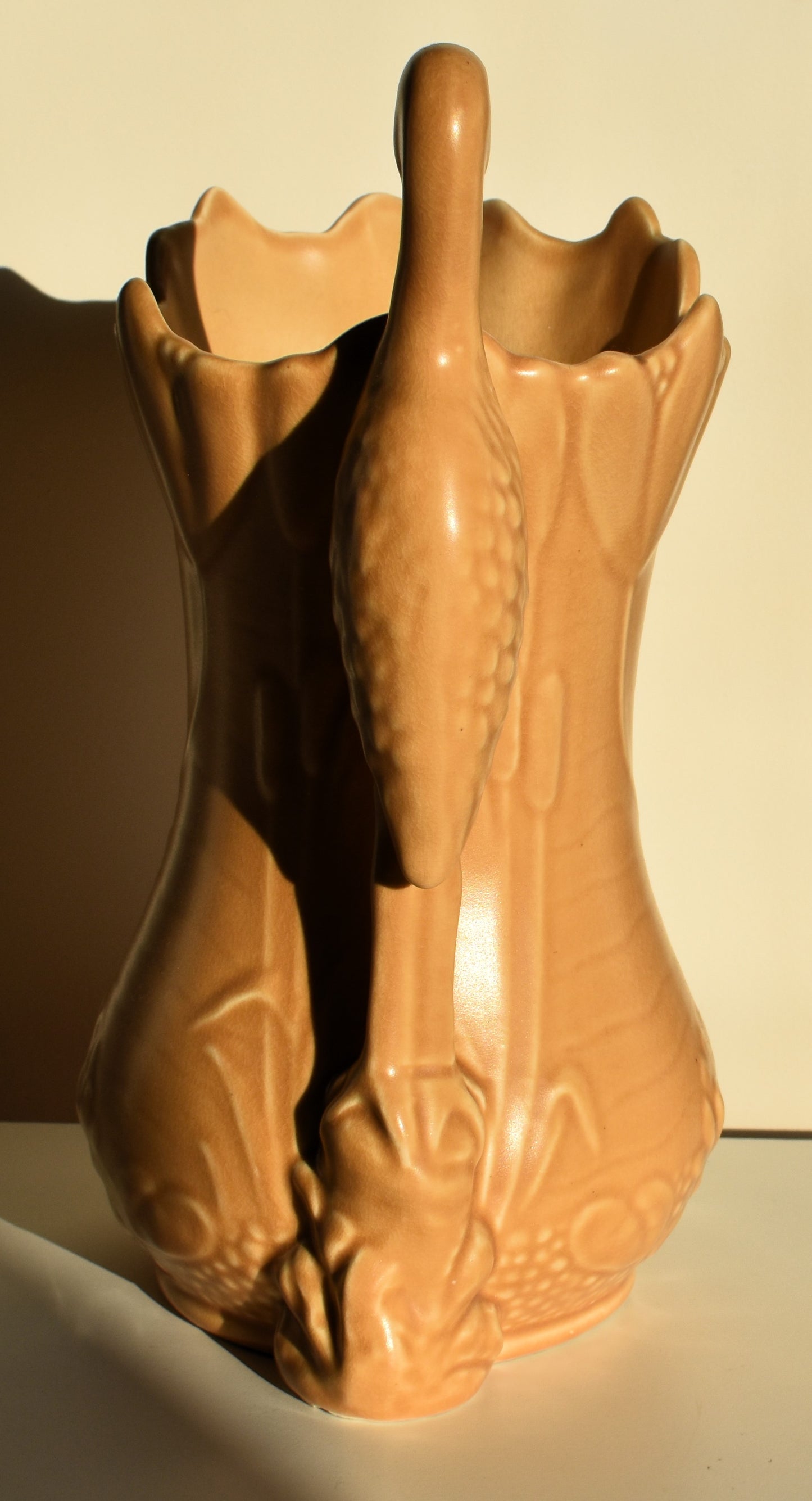 A caramel coloured vase decorated with lilies and tulips has a stork for a handle.