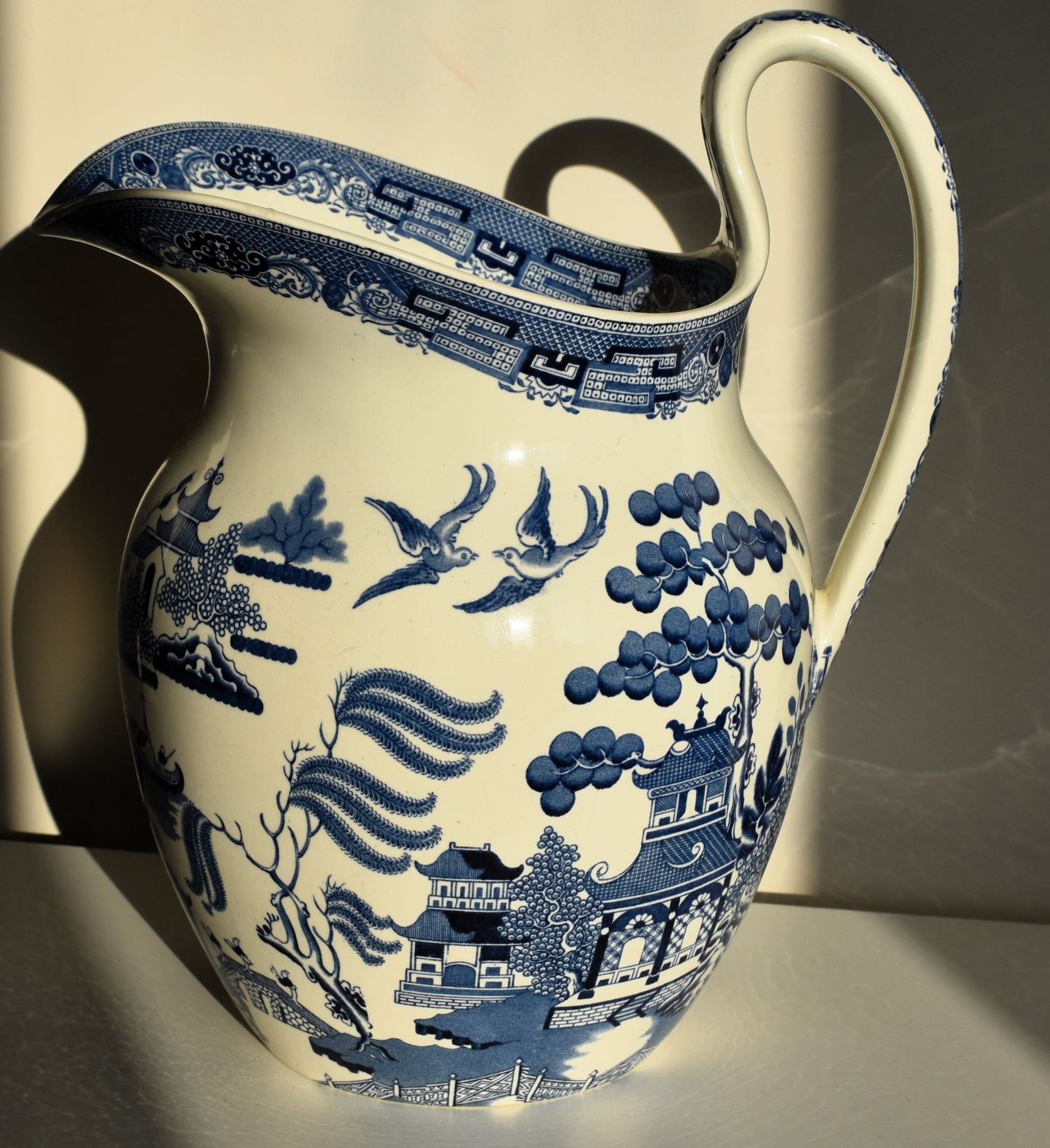 A large pitcher style jug is decorated in classic willow pattern, in blue and white