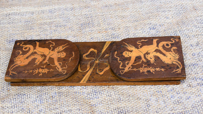 Wooden decorative panel with intricate carvings of cherubs and ribbons on a textured fabric background.