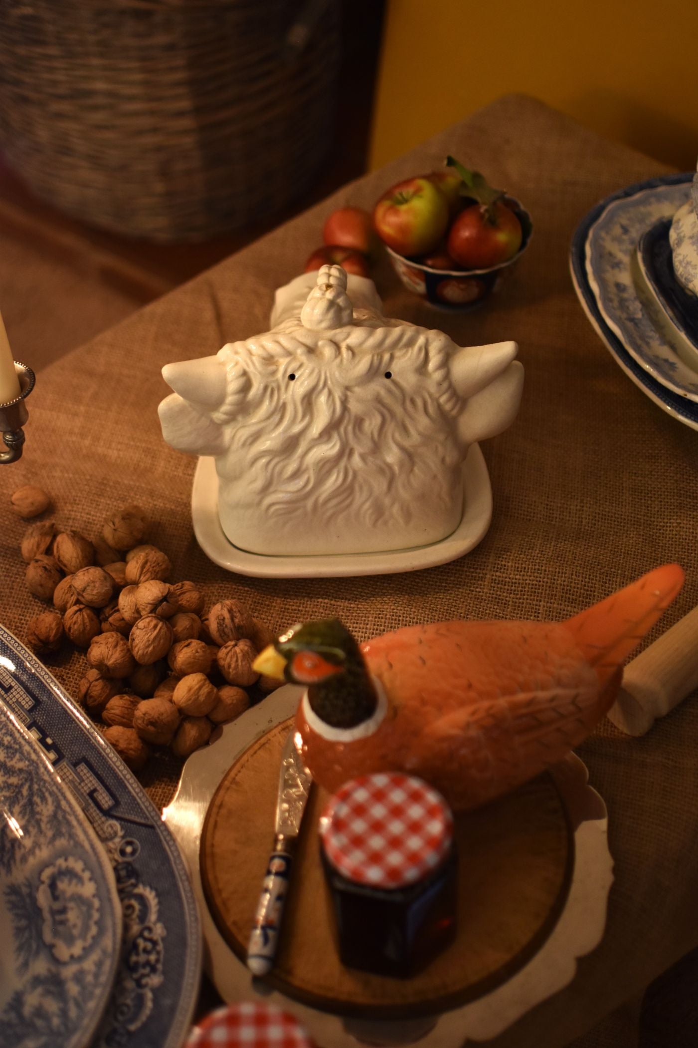 A serving dish in the shape of a bull or cow's head in the middle of a table also showing jam, walnuts and apples on a brown hessian 