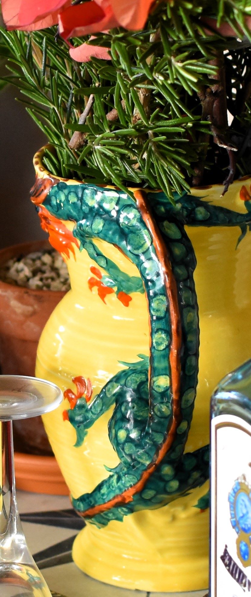 A yellow jug is decorated with an art deco dragon. The dragon's body is green and its head, tail and claws are red. The dragon's body is the handle of the jug