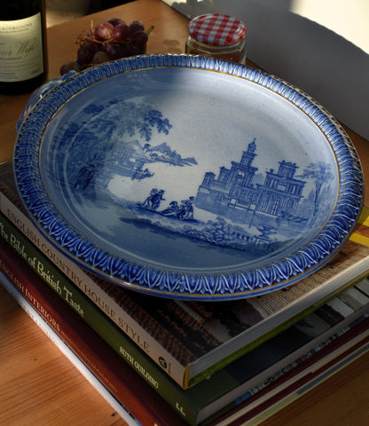 Blue decorative plate with a scenic design on top of books