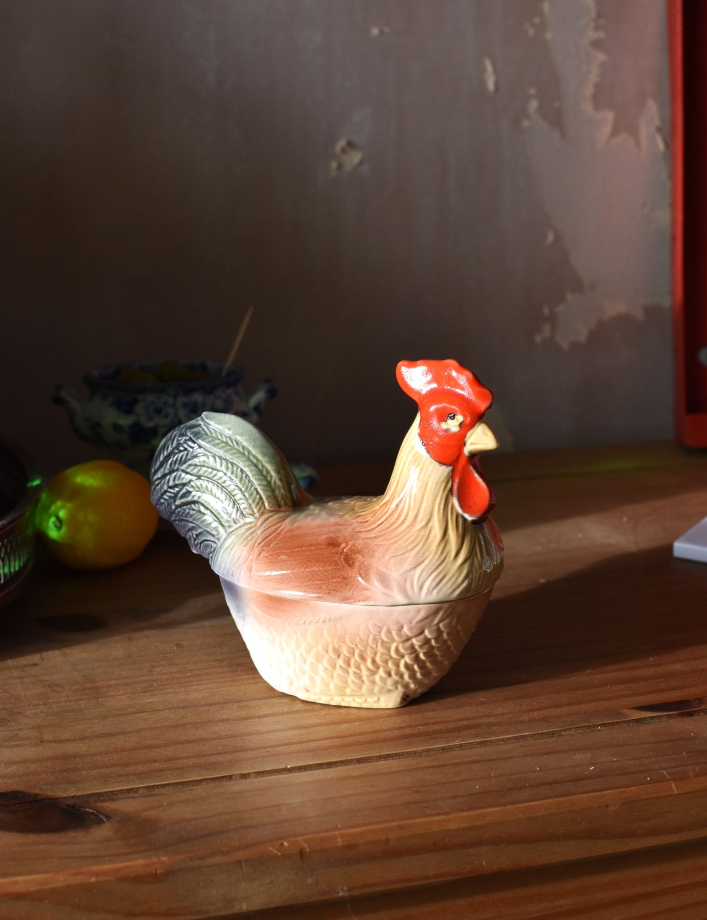 a small covered dish in the shape of a cockerel or rooster on a wooden table