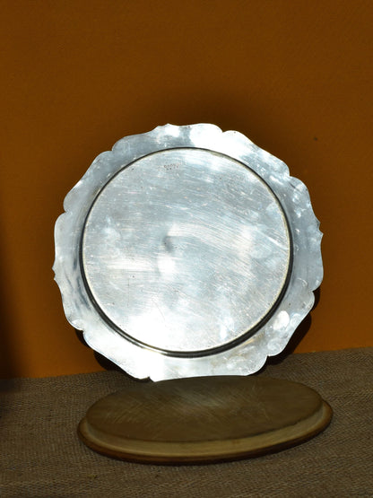 Decorative silver plate with a textured edge on a wooden stand against an orange background