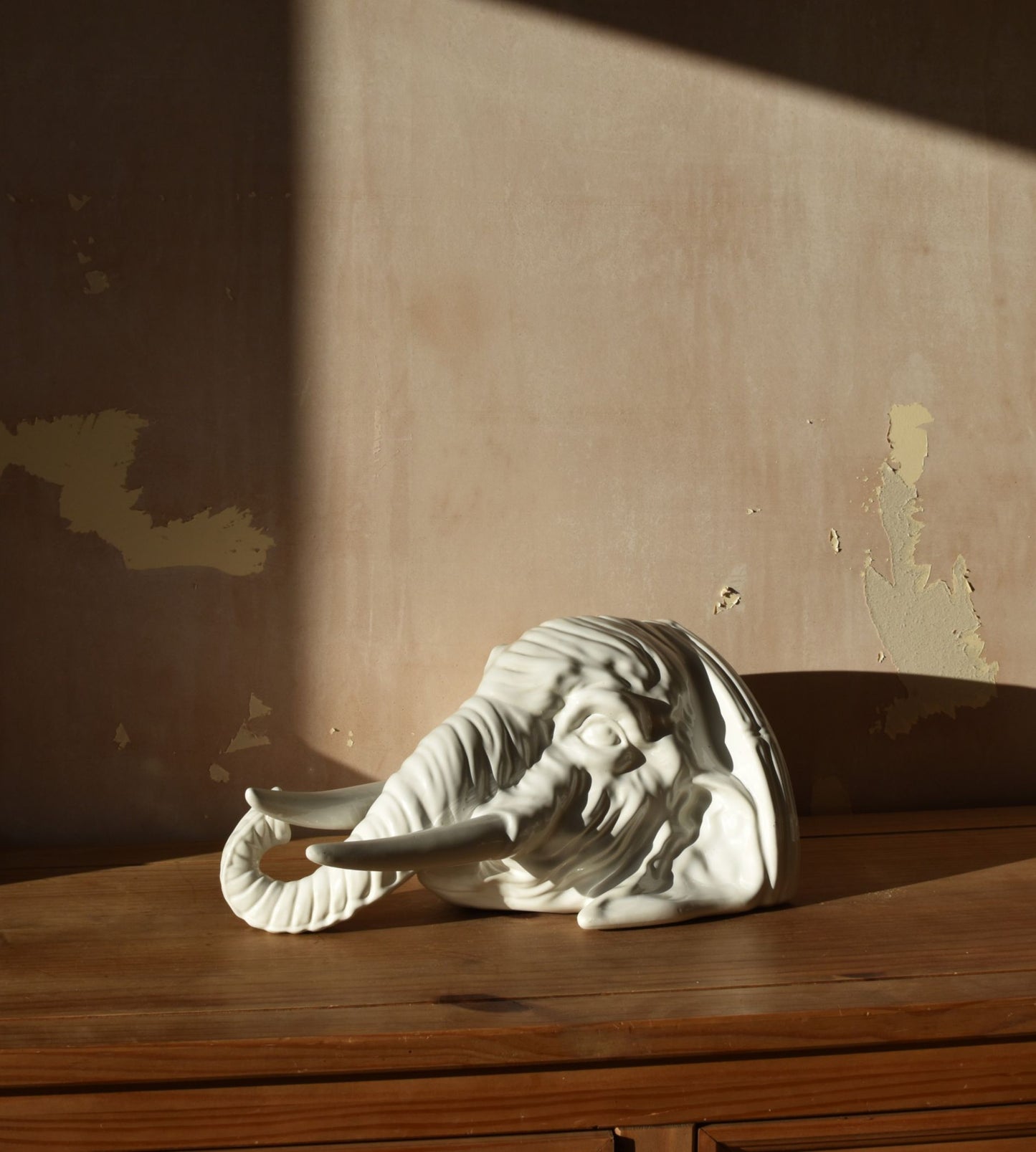A large white porcelain elephant head is against a pink background