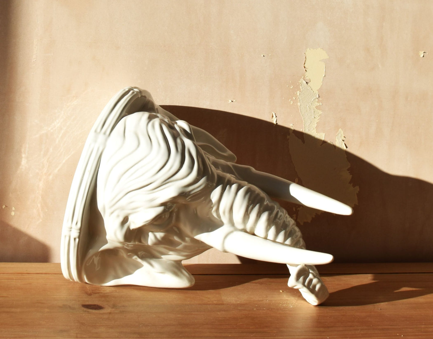 A large white porcelain elephant head is against a pink background