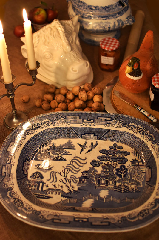 Decorative blue and white platter with intricate Willow pattern on a table with candles and food.