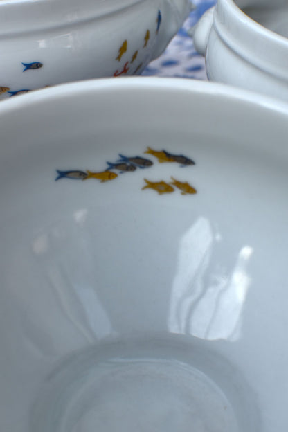 Close-up of a white ceramic bowl with fish illustrations on a patterned surface.