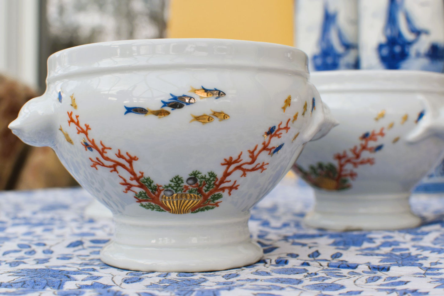 White ceramic bowl with colorful coral and fish design on a blue and white patterned tablecloth.