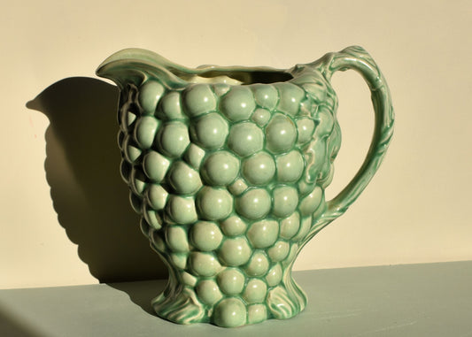 Green ceramic pitcher with grape design on a beige background