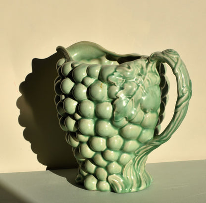 Green ceramic pitcher shaped like a bunch of grapes on a neutral background