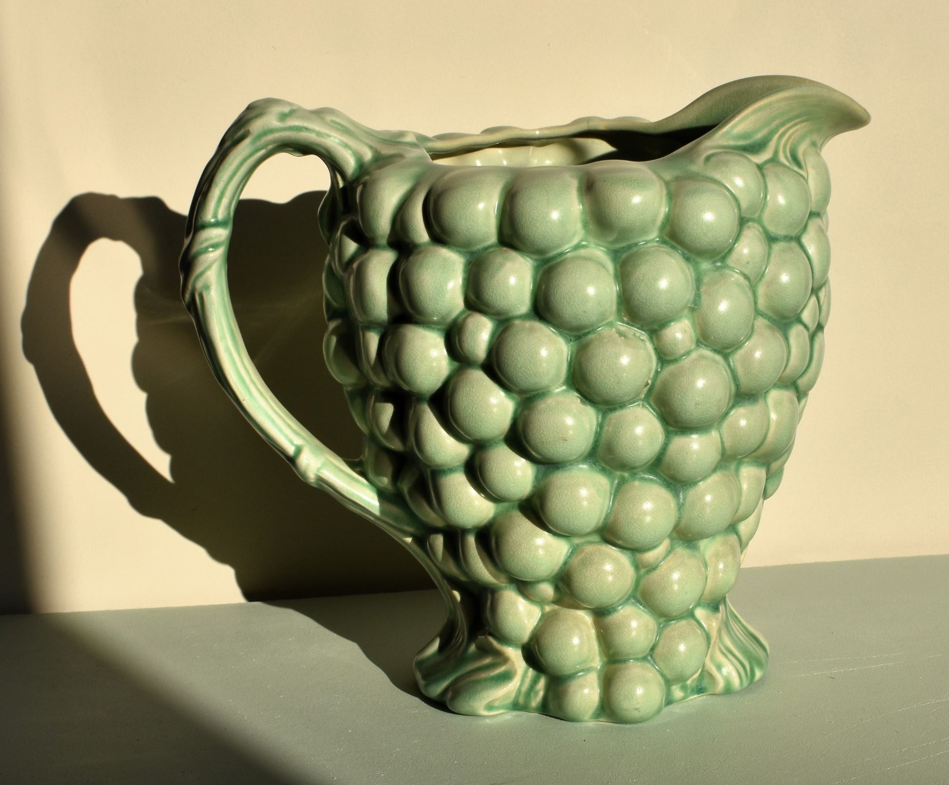 Green ceramic pitcher with grape design on a neutral background