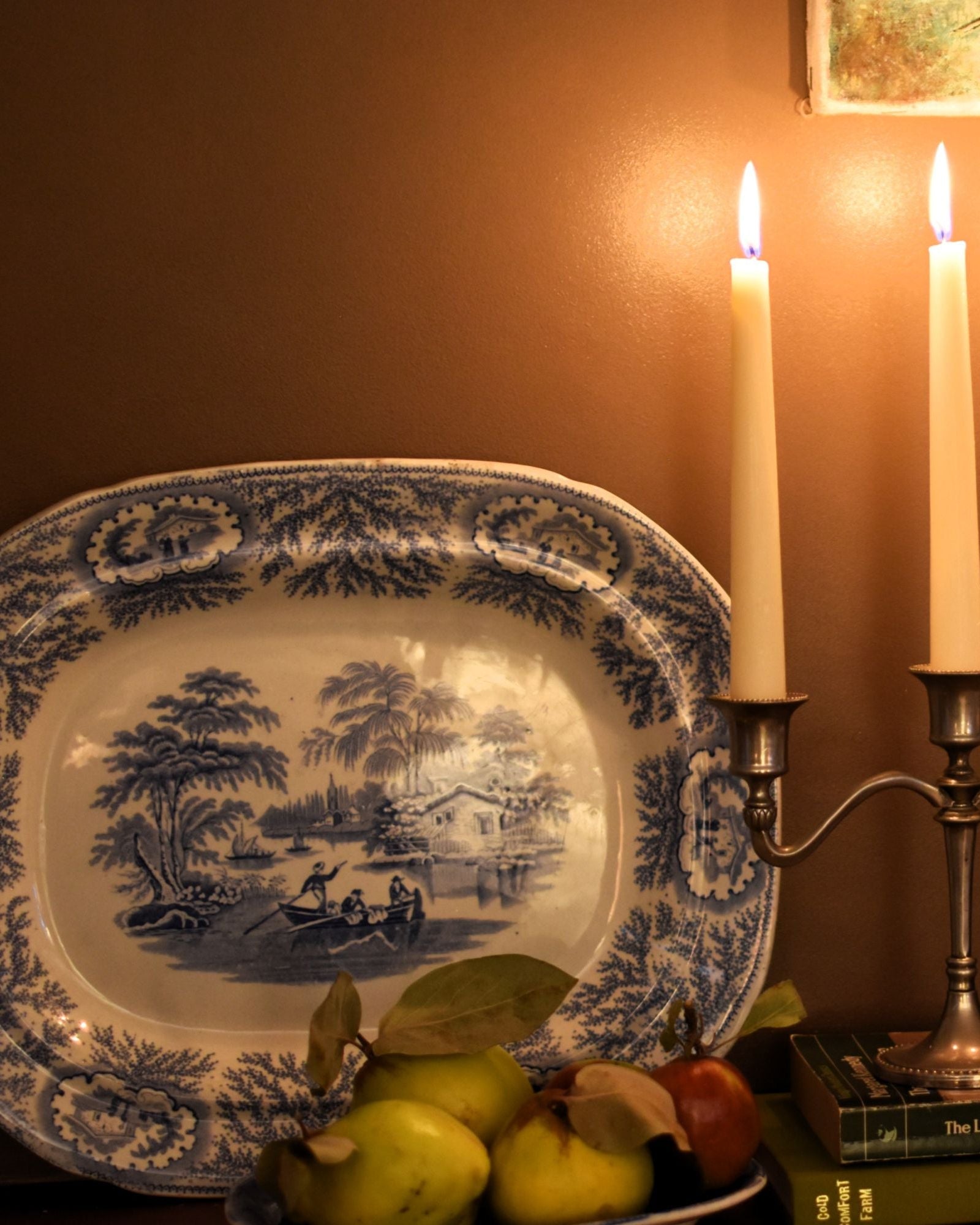 Decorative setting with candles, platter, and vases against a brown wall.