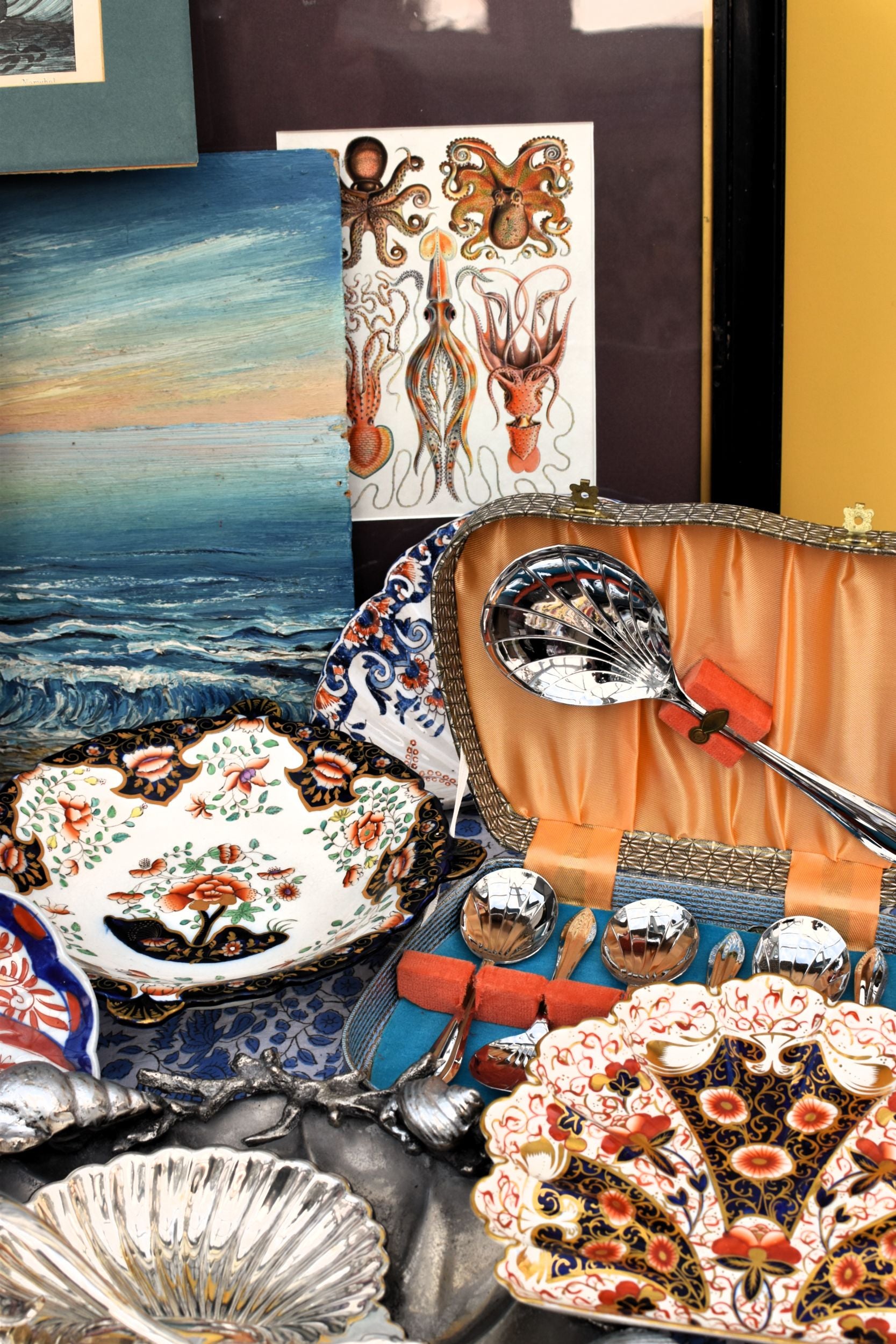 Collection of decorative plates and a ladle on a table with a scenic painting in the background.