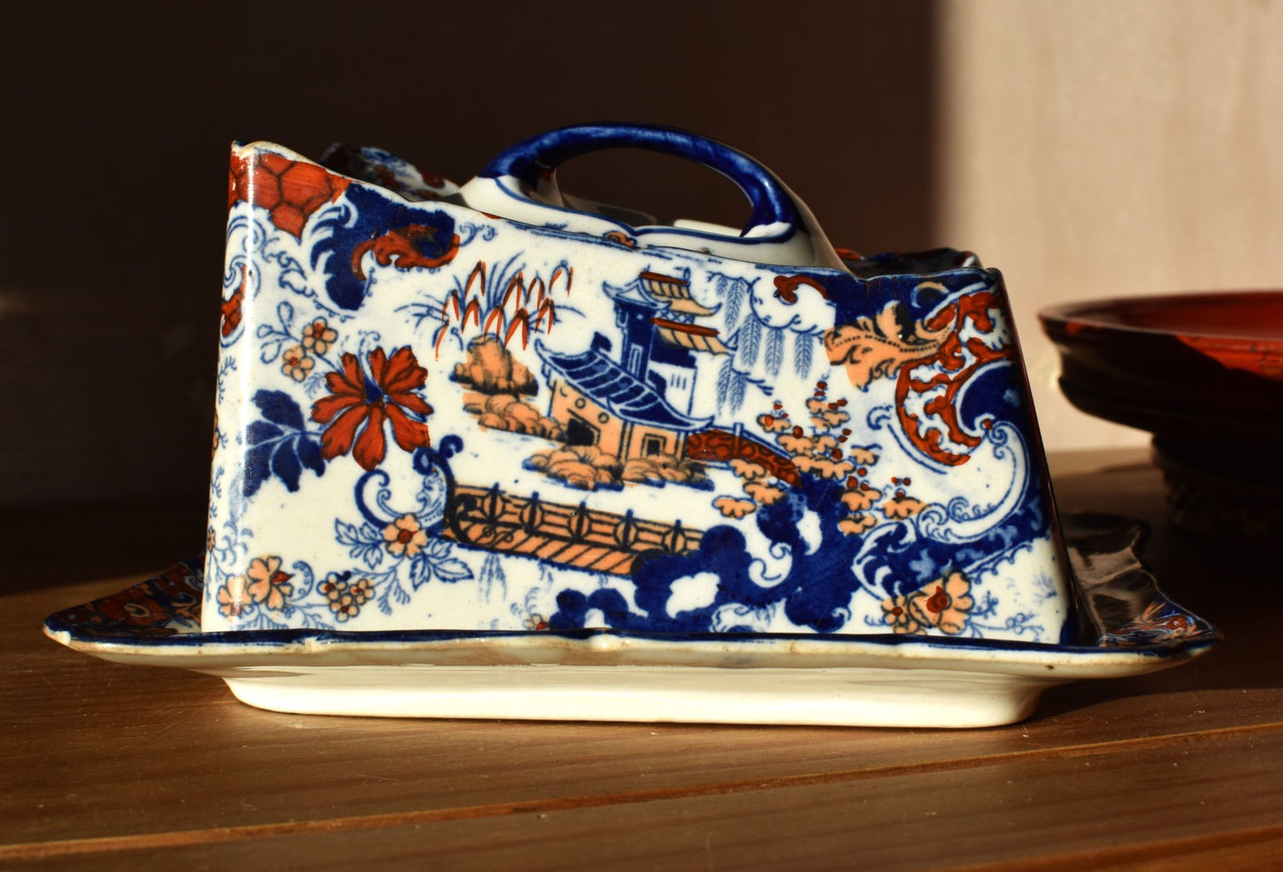 A blue and orange floral decorated covered dish against a red and pink background