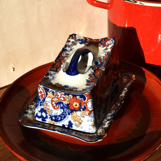 A blue and orange floral decorated covered dish against a red and pink background