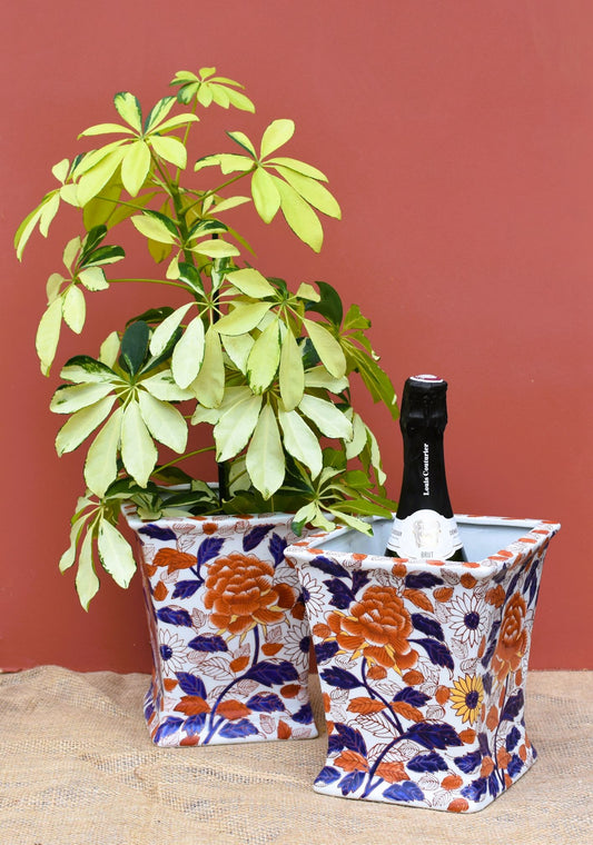 Decorative plant pot with a bottle of champagne on a floral ice bucket against a red background