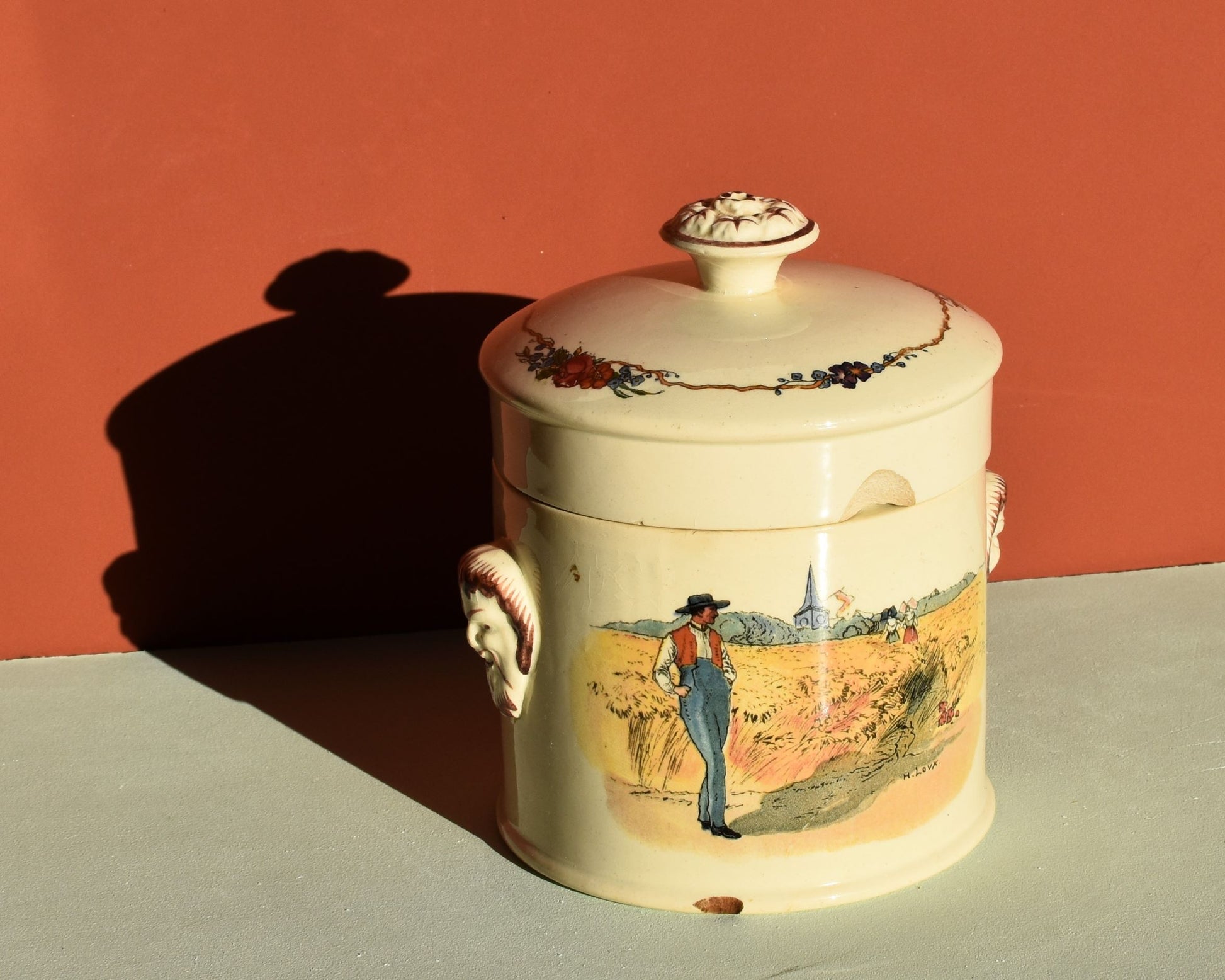 Decorative ceramic jar with lid on a flat surface against an orange wall