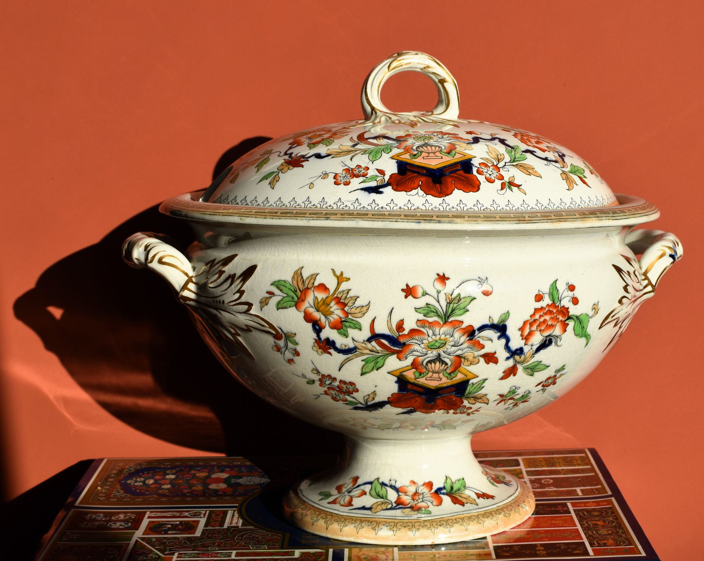 Large white footed tureen painted with red, blue and green floral decoration, against a red background