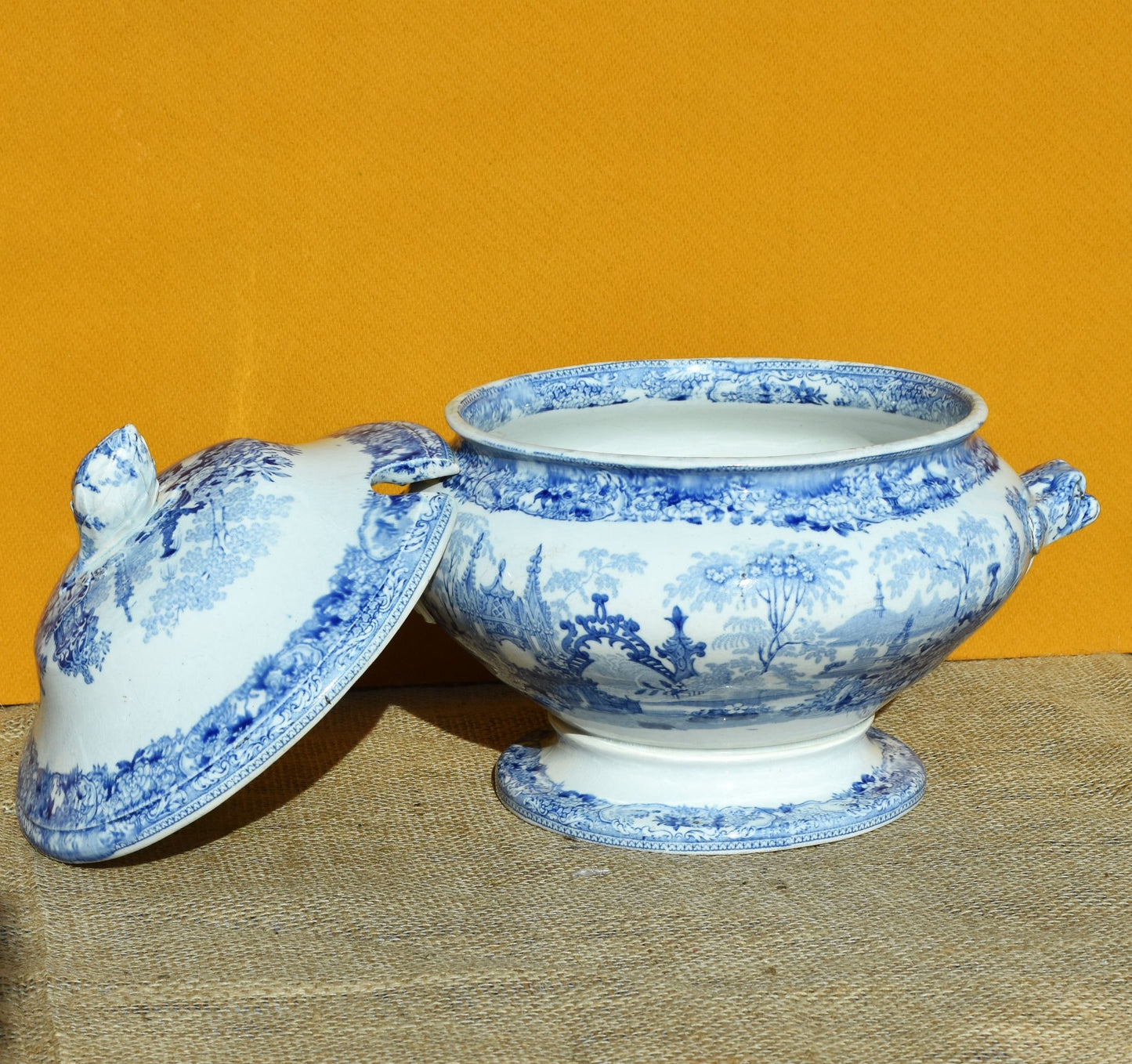 Blue and white ceramic tureen with lid on a textured surface against an orange background