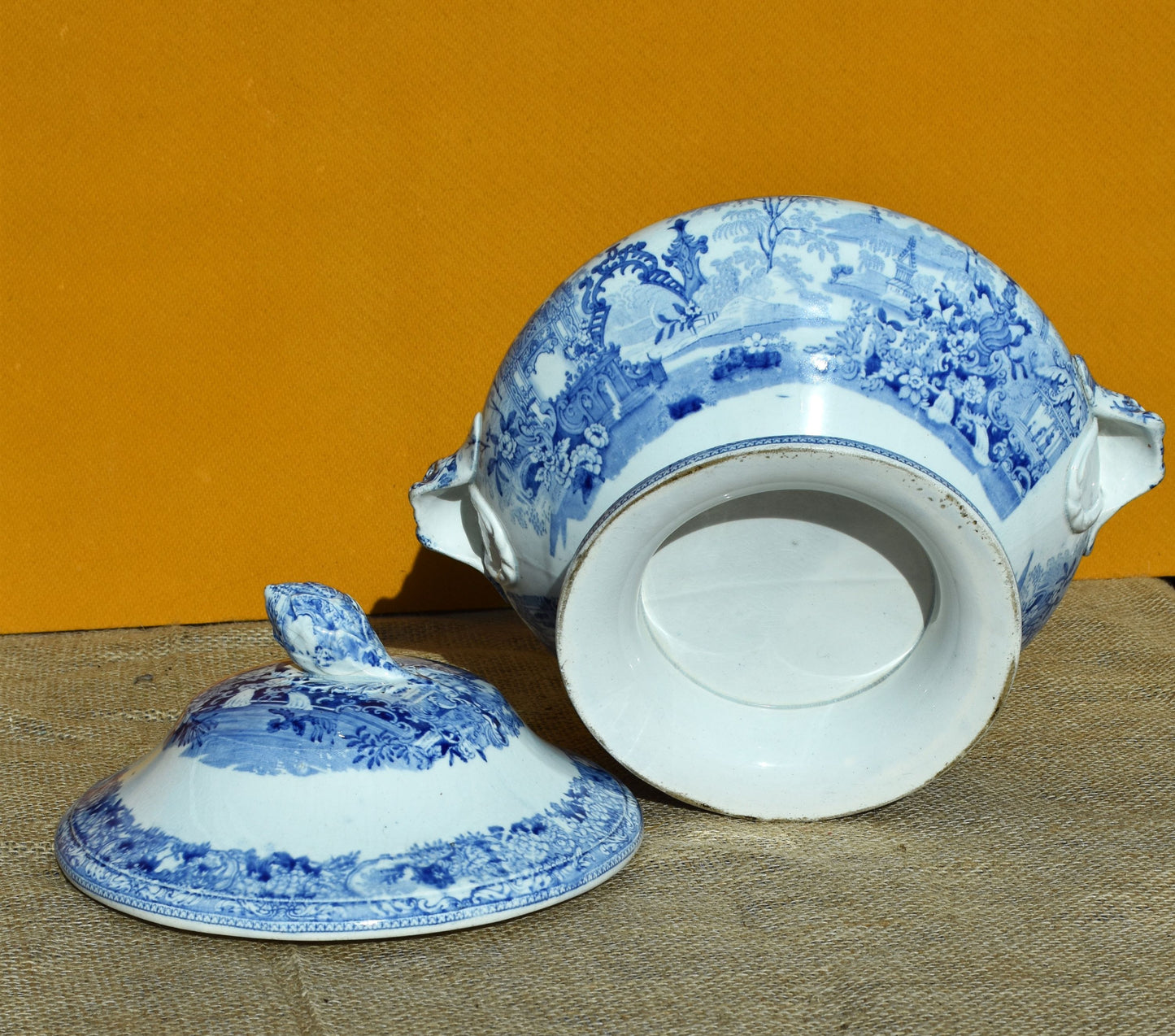 Blue and white ceramic tureen with lid on a textured surface against an orange background