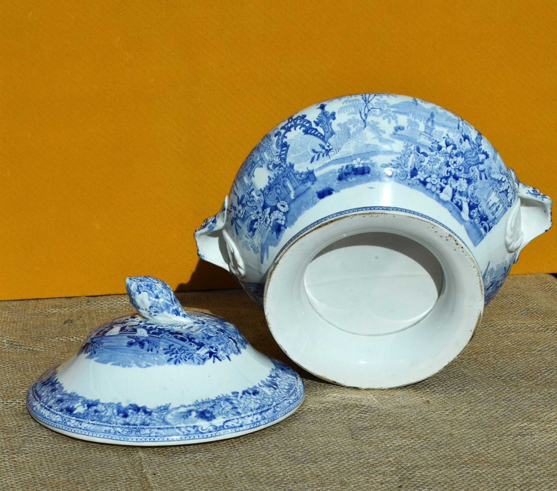Blue and white ceramic tureen with lid on a textured surface against an orange background