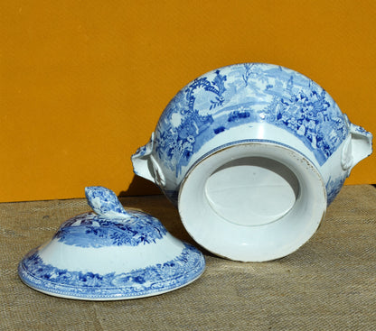 Blue and white ceramic tureen with lid on a textured surface against an orange background