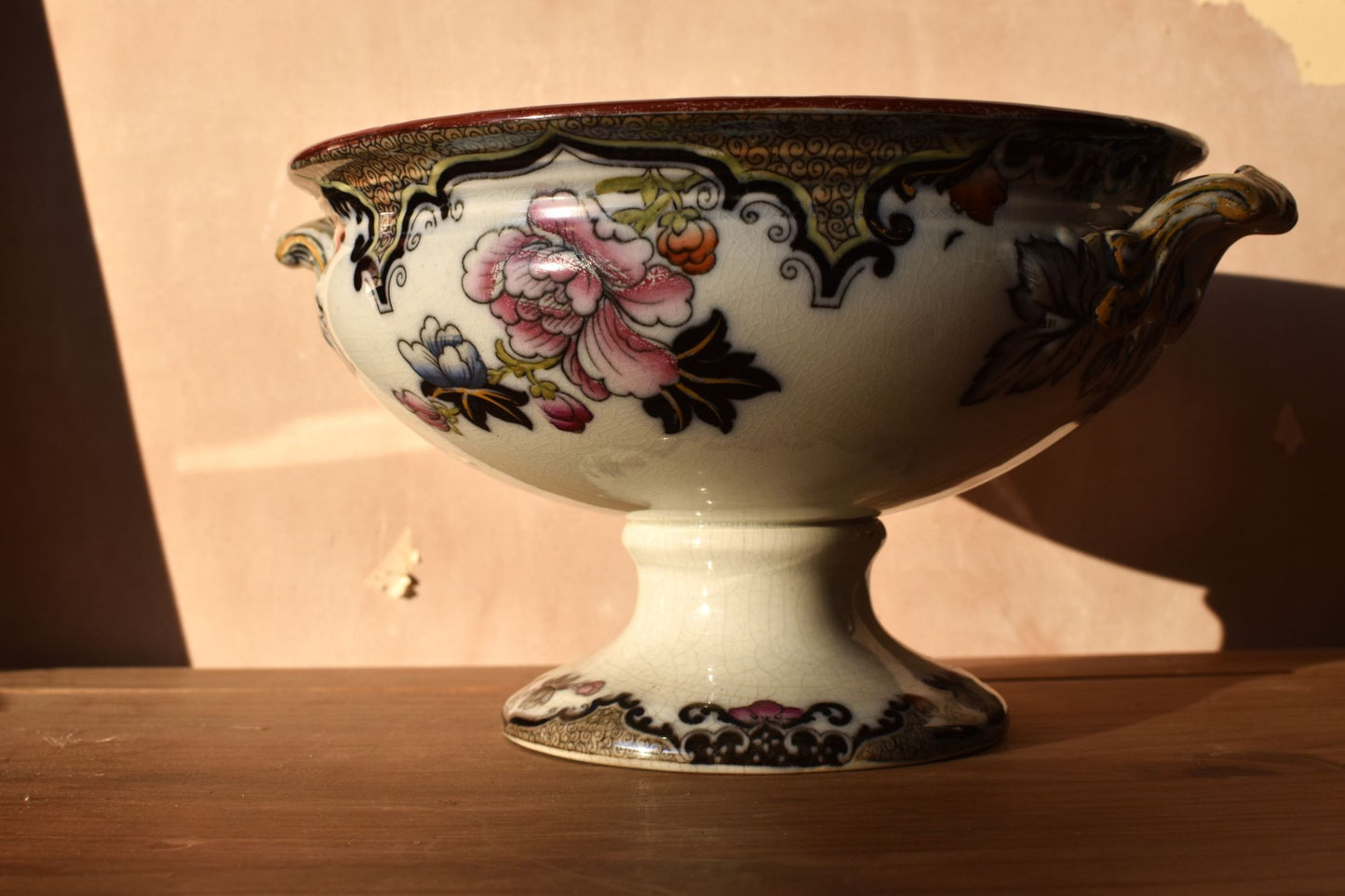 Art nouveau ceramic bowl with hand painted floral patterns on a wooden surface