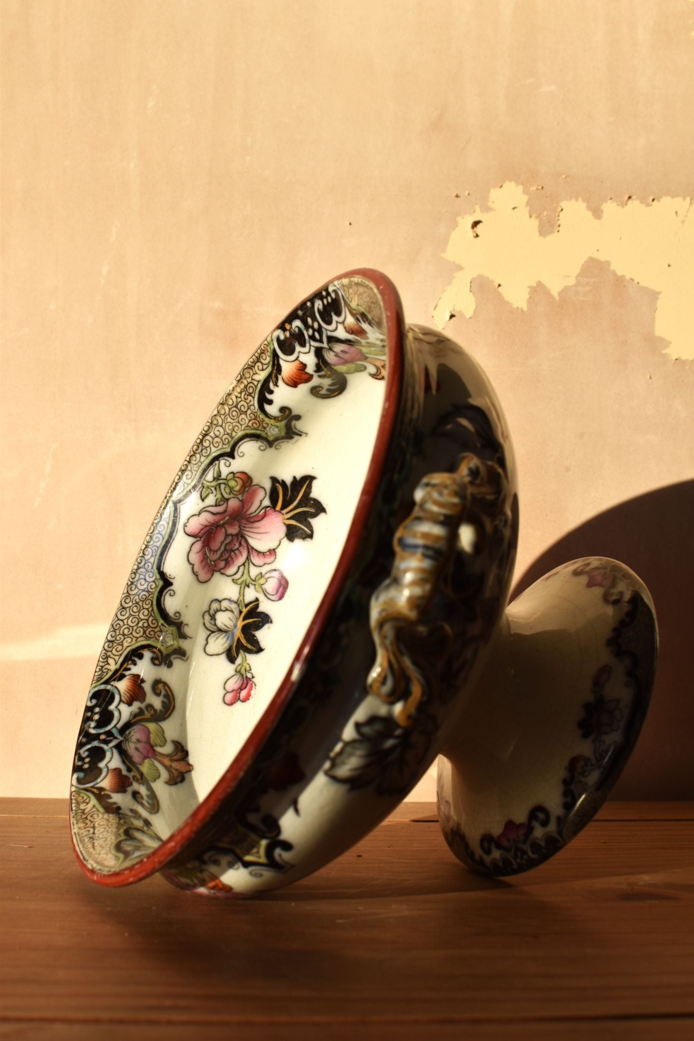 Decorative ceramic pedestal bowl with floral and animal designs on a wooden surface.