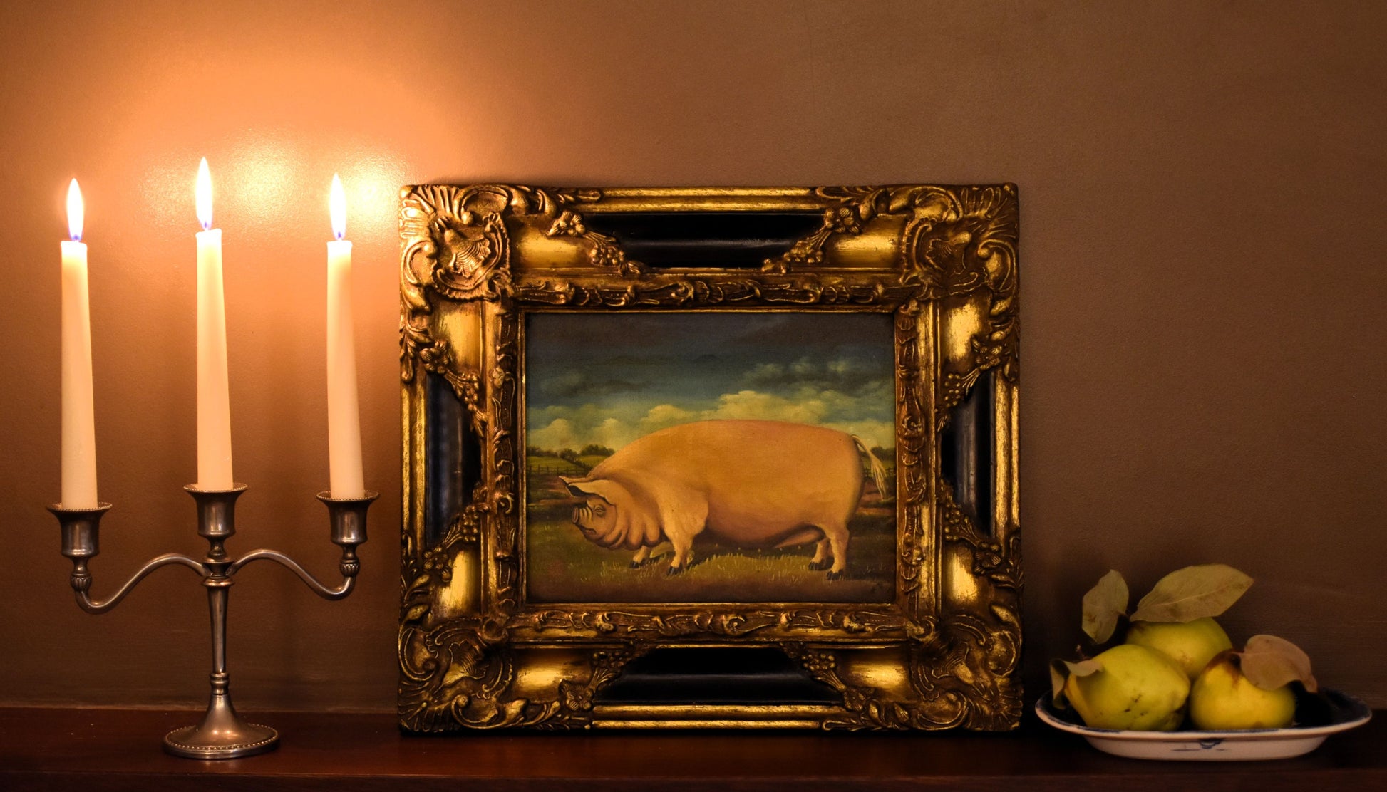 Oil painting of a large pink pig in a carved and gold gilded frame, lit by candlelight